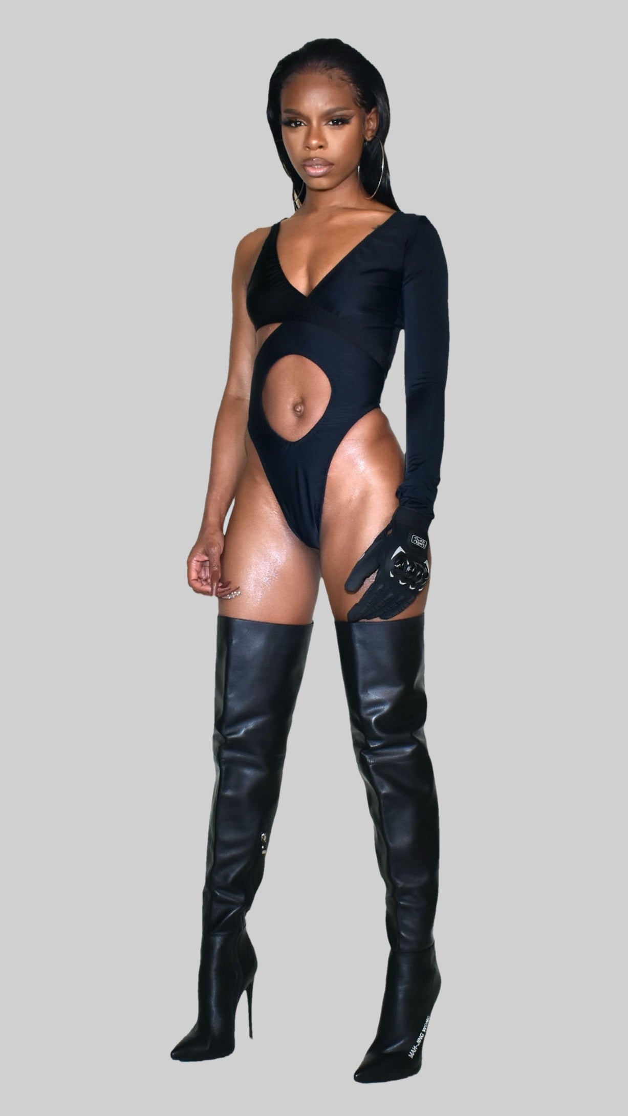 Person wearing a black bodysuit with cut-out design and black knee-high boots on a gray background